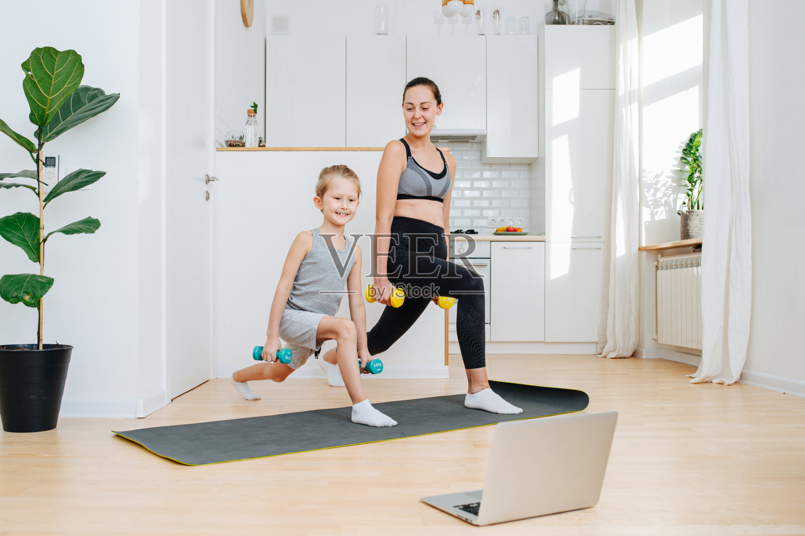 自豪的母亲和儿子在家里的笔记本电脑前举着哑铃锻炼照片摄影图片
