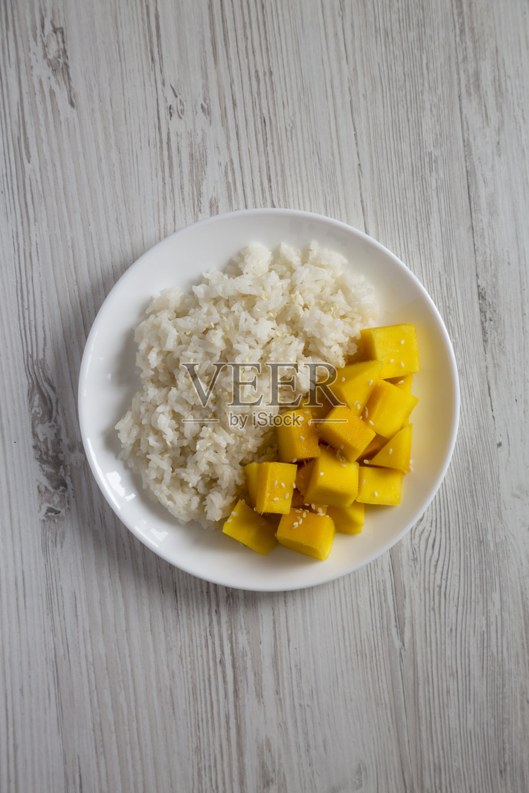 自制的芒果芝麻糯米饭放在白色的盘子里，白色的木桌上，俯视图。平躺着，头顶上，从上面。照片摄影图片