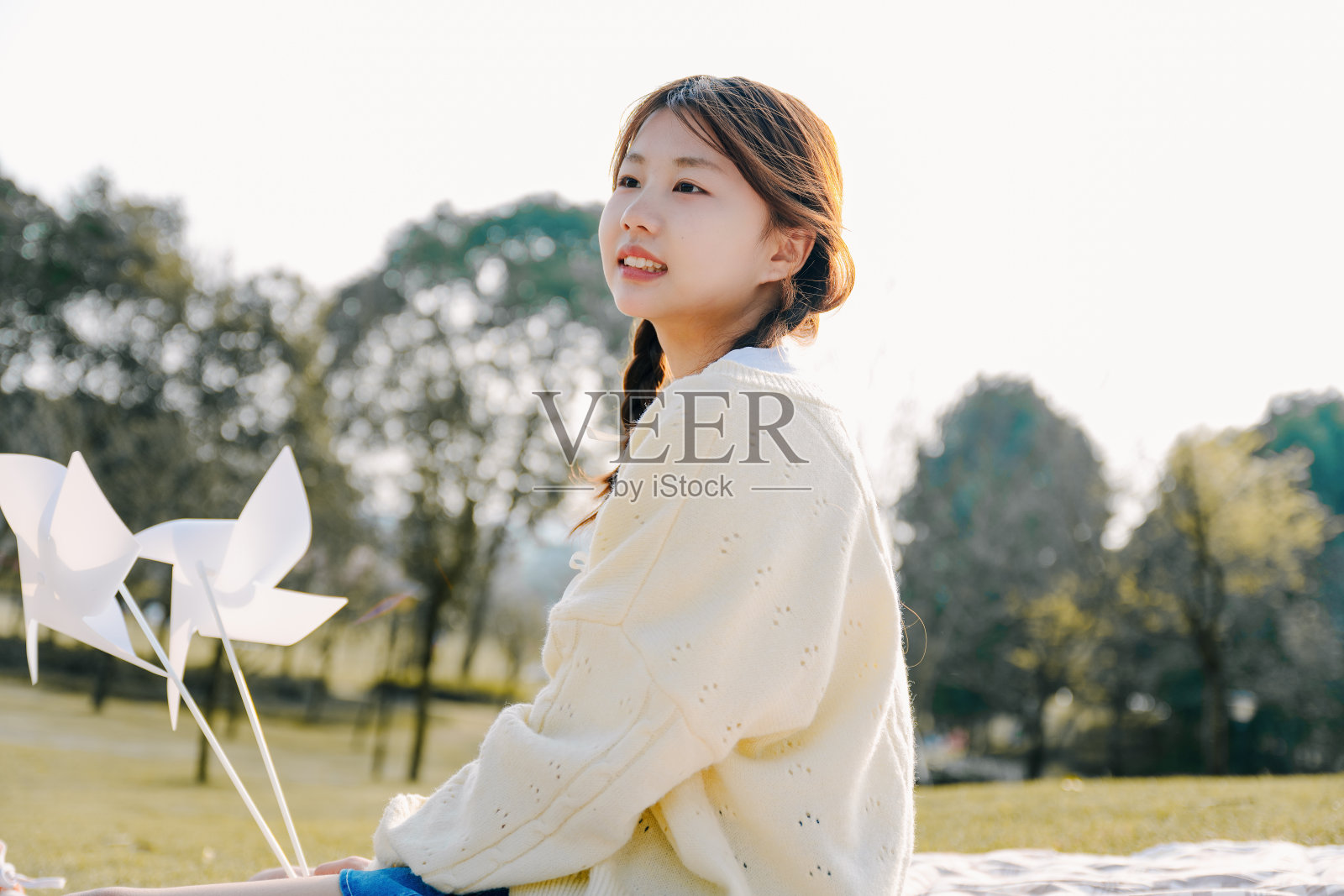 一个美丽的亚洲女孩坐在毯子上在一个阳光明媚的日子玩纸风车照片摄影图片