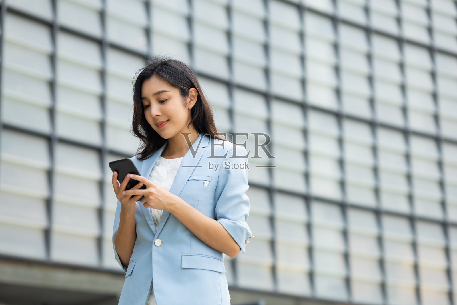 漂亮的女商人用手机在市中心的建筑物里玩社交媒体。聪明的女性使用手机聊天进行商务沟通。智能手机的概念。照片摄影图片