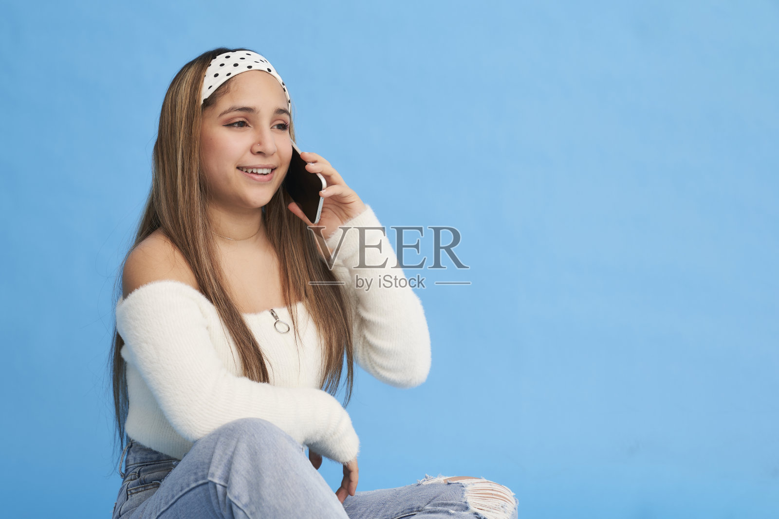 一位年轻的西班牙裔妇女坐在地板上打电话的肖像照片摄影图片