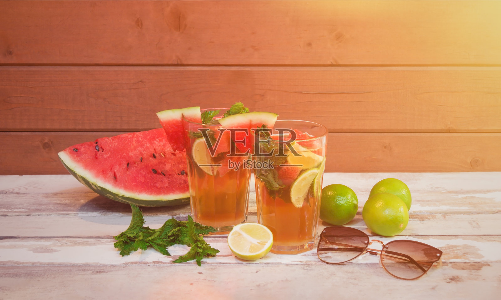 木桌上放着西瓜莫吉托鸡尾酒和太阳镜。附近有西瓜、酸橙和薄荷。照片摄影图片