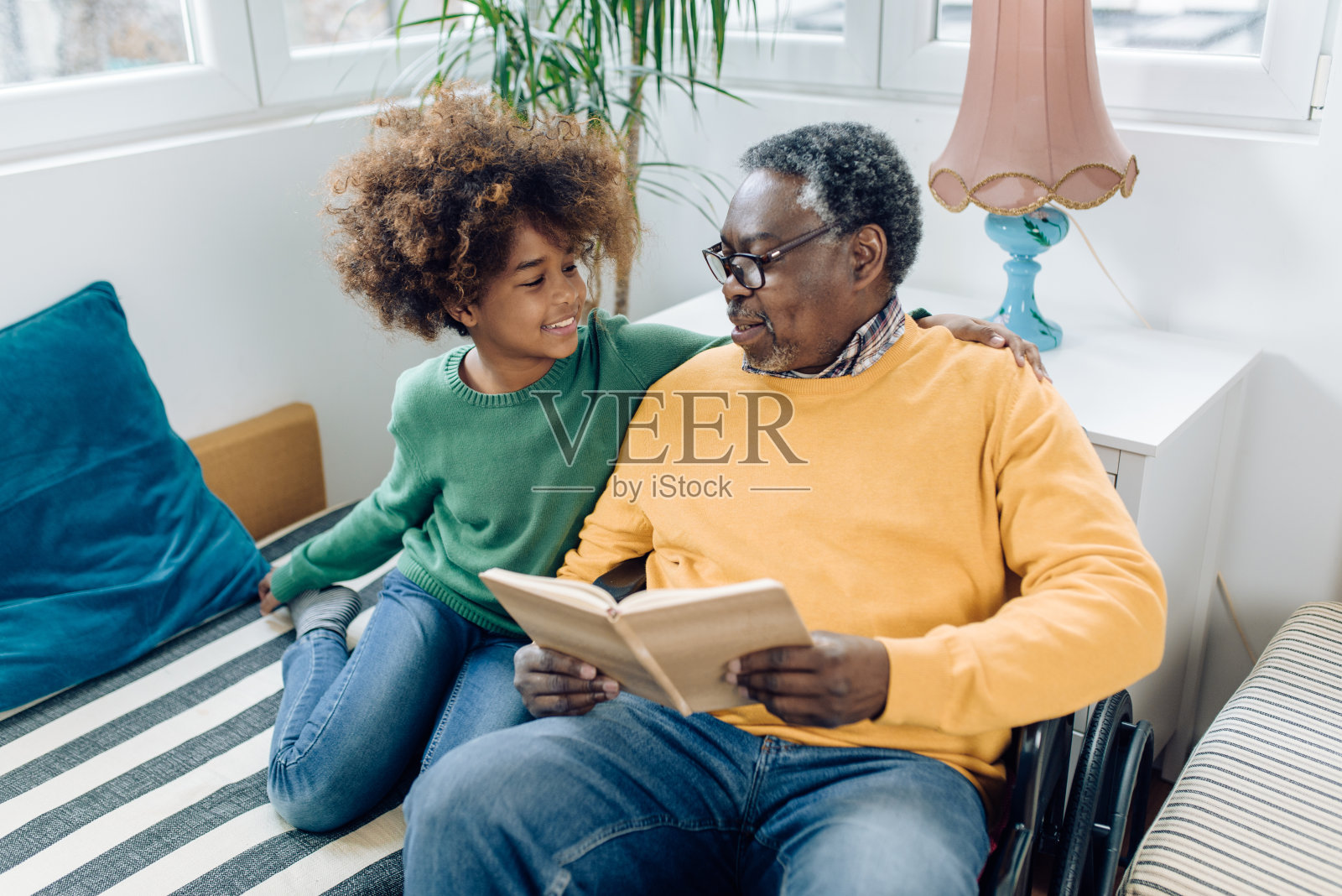 快乐的非裔美国女孩和坐在轮椅上的爷爷一起读故事照片摄影图片