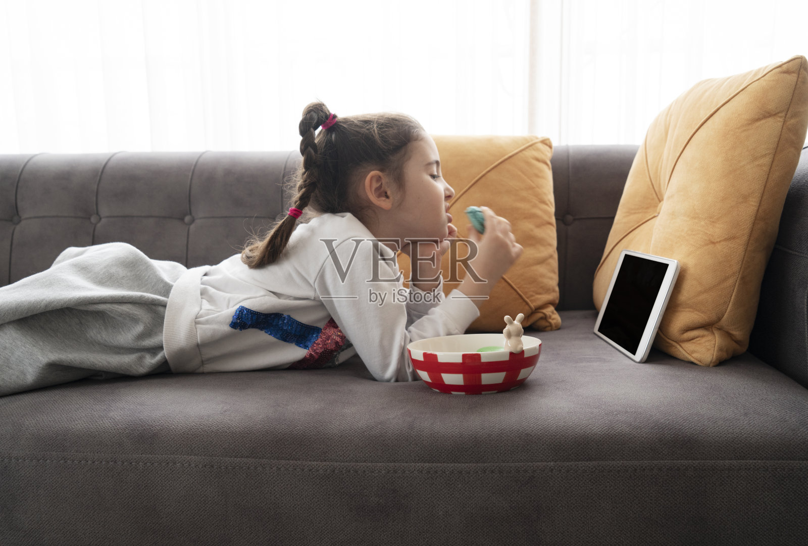 可爱的小女孩吃着杏仁饼干，用着数码平板电脑照片摄影图片