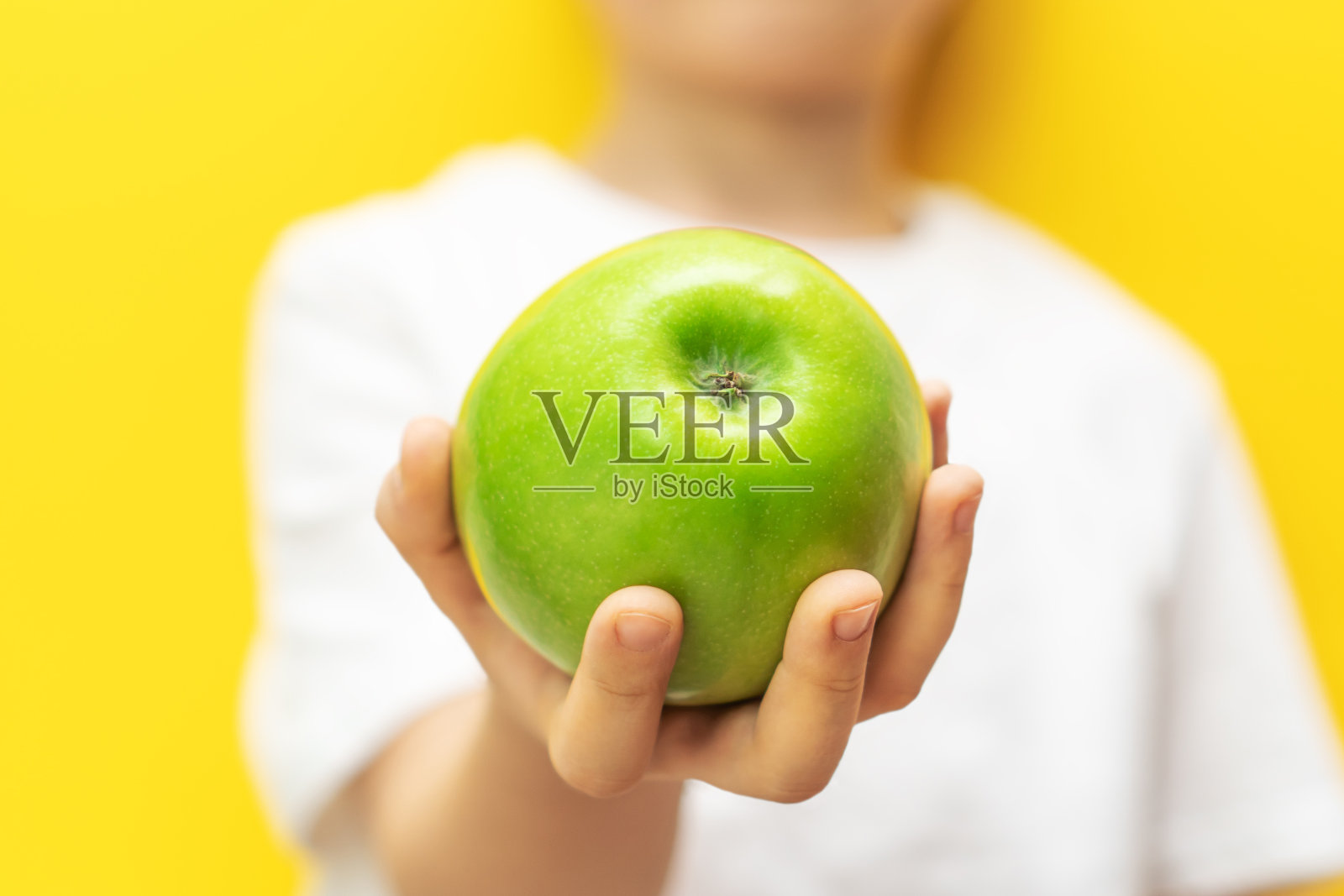 孩子在欢快的黄色背景上放着鲜绿的苹果。孩子模糊的身影。关注苹果。照片摄影图片