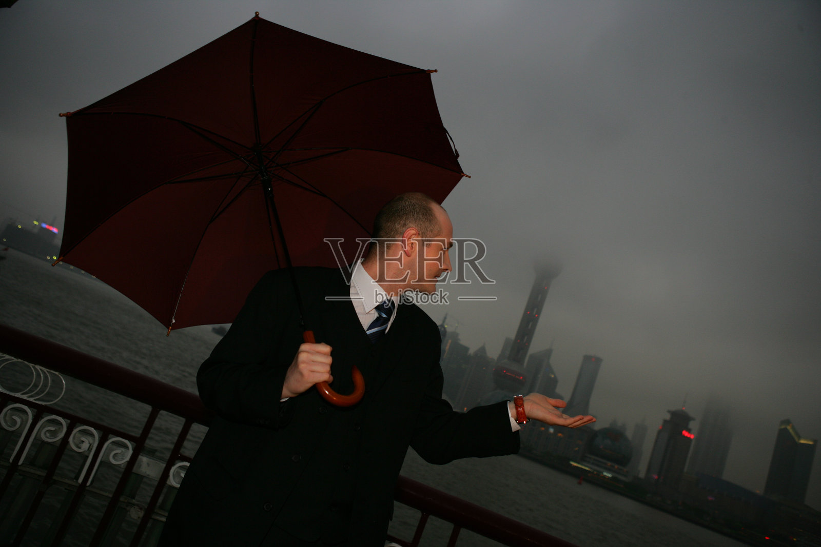 阴雨天外滩黄浦江边一位外国商务人士拿伞伸手接雨照片摄影图片