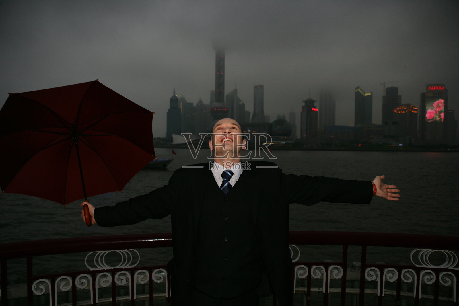 阴雨天外滩黄浦江边一位外国商务人士拿伞张开双臂照片摄影图片