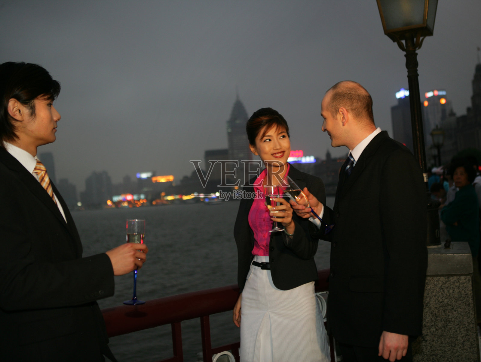 傍晚外滩黄浦江边三位中外商务人士端酒杯交谈照片摄影图片