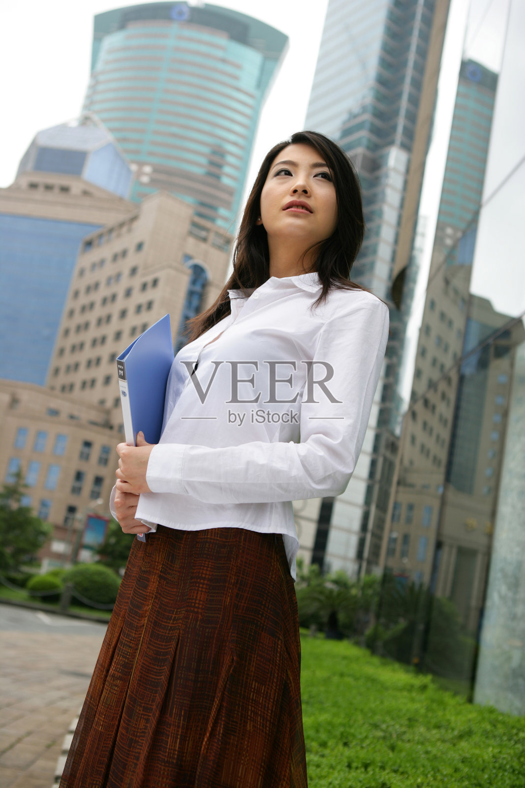 上海浦东写字楼旁一位女商务人士拿文件夹站立照片摄影图片