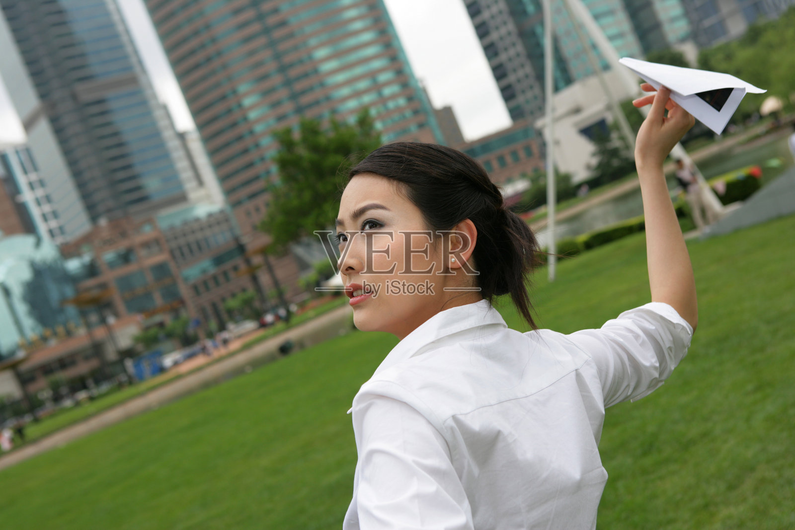 上海浦东写字楼旁草坪上一位女商务人士玩纸飞机照片摄影图片