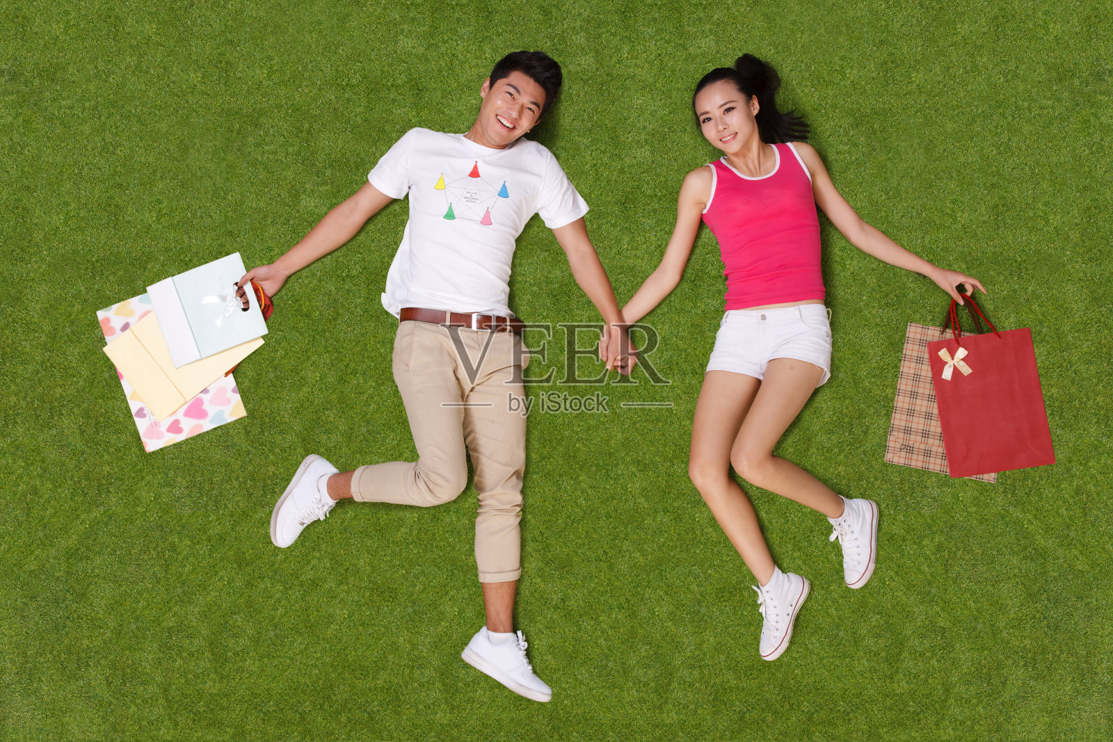 青年男女手提购物袋躺在草地上照片摄影图片