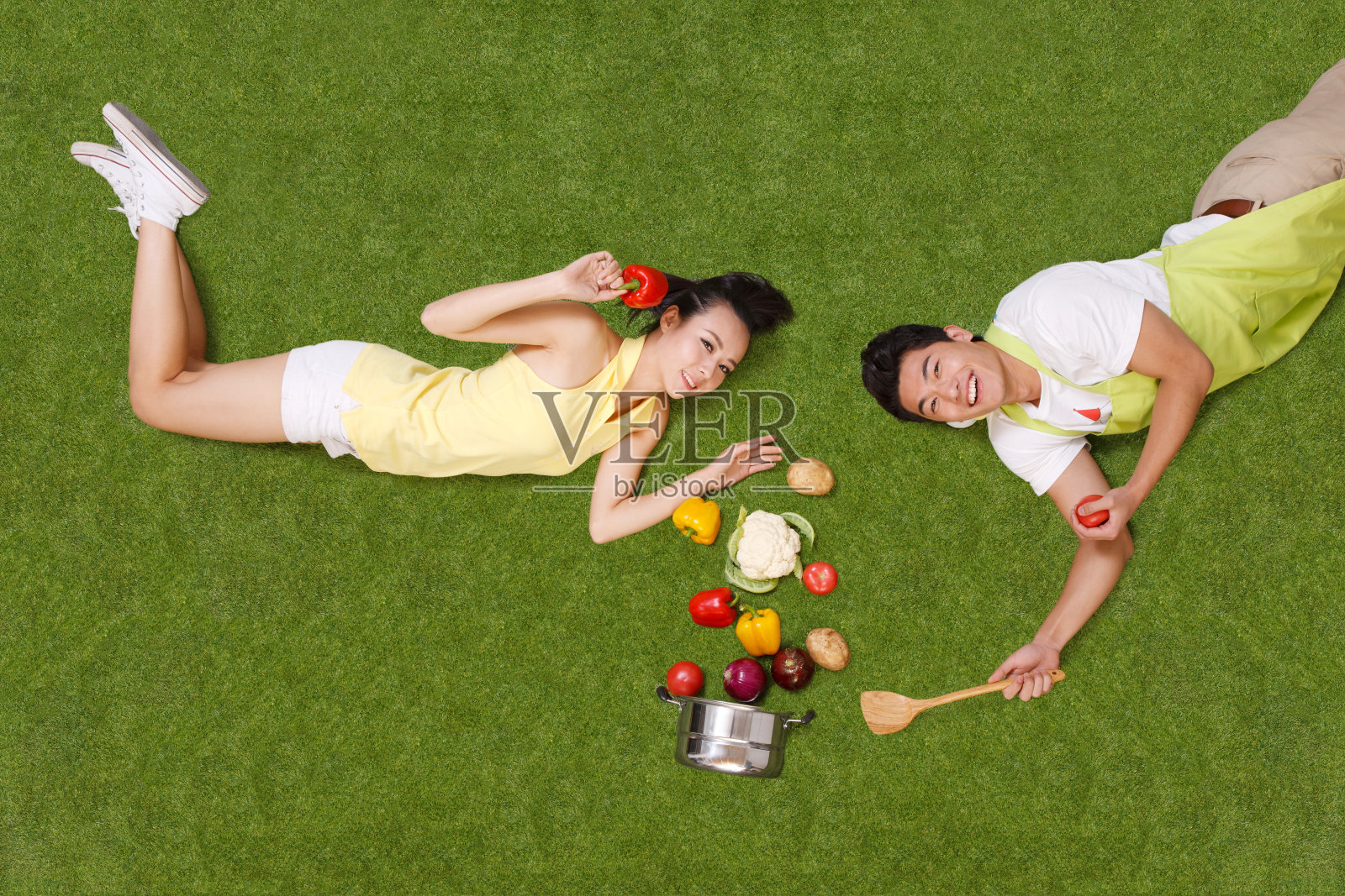 青年男女拿着蔬菜躺在草地上照片摄影图片