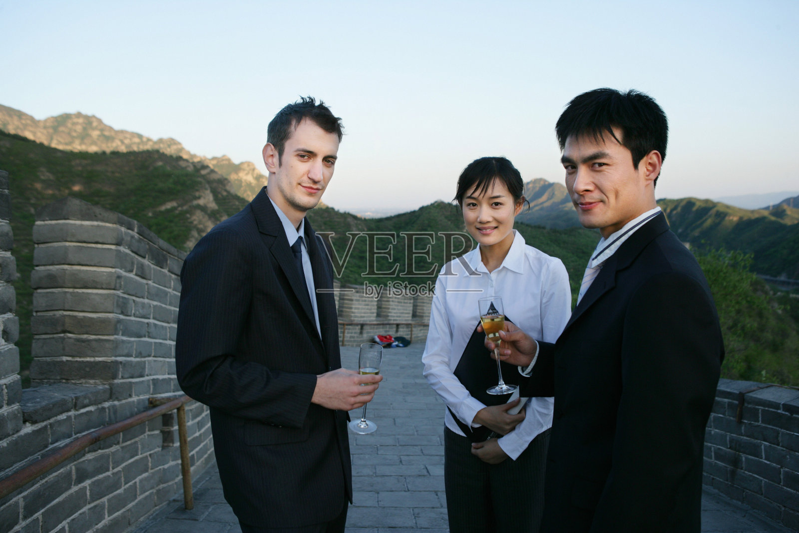 三位中外商务人士在长城上端酒杯站立照片摄影图片