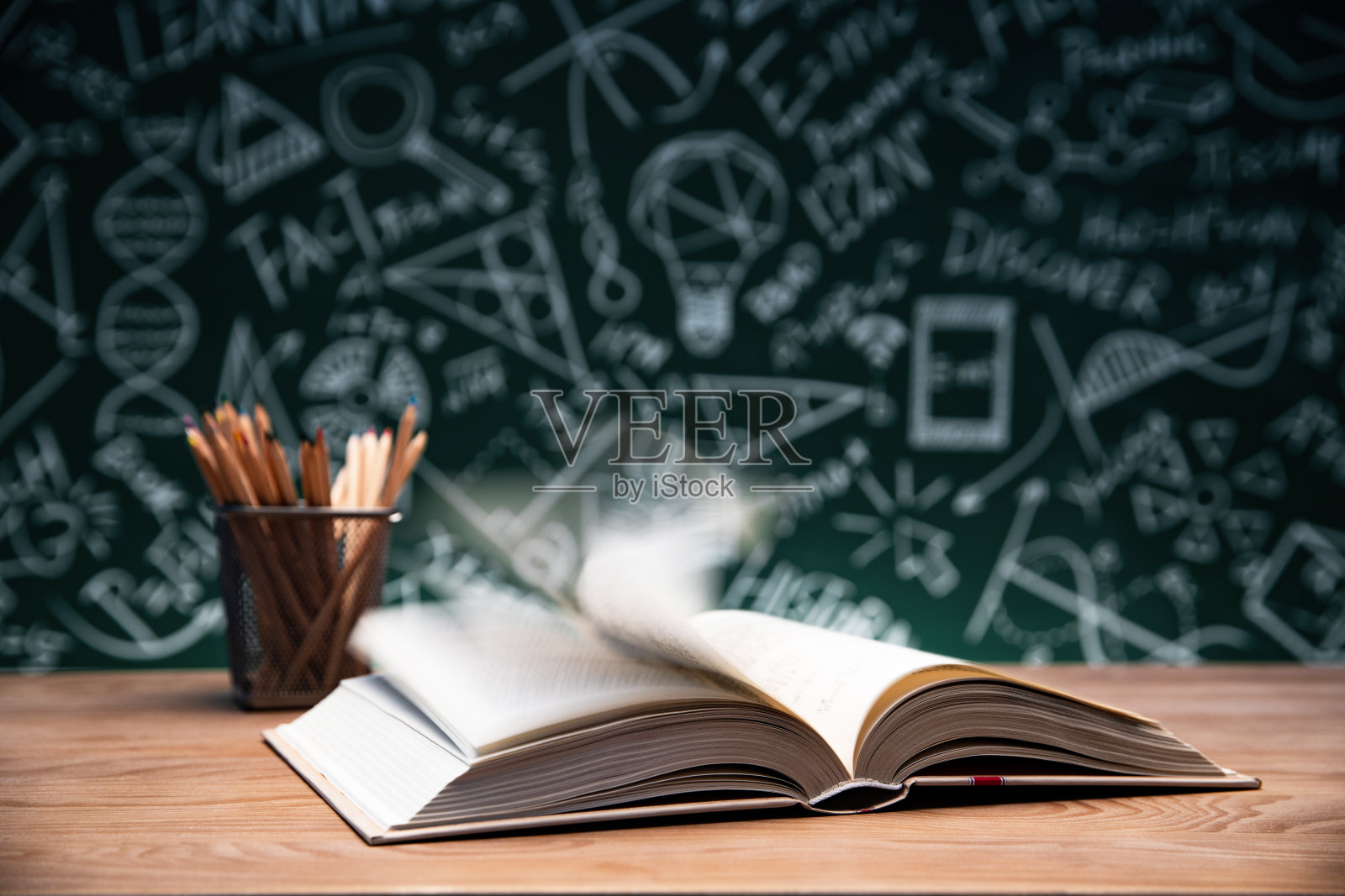黑板画前的桌子上打开的书和笔筒照片摄影图片