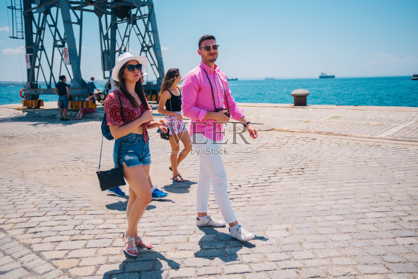 在一个阳光明媚的夏日，游客们在现代城市的木板路上观光散步。照片摄影图片