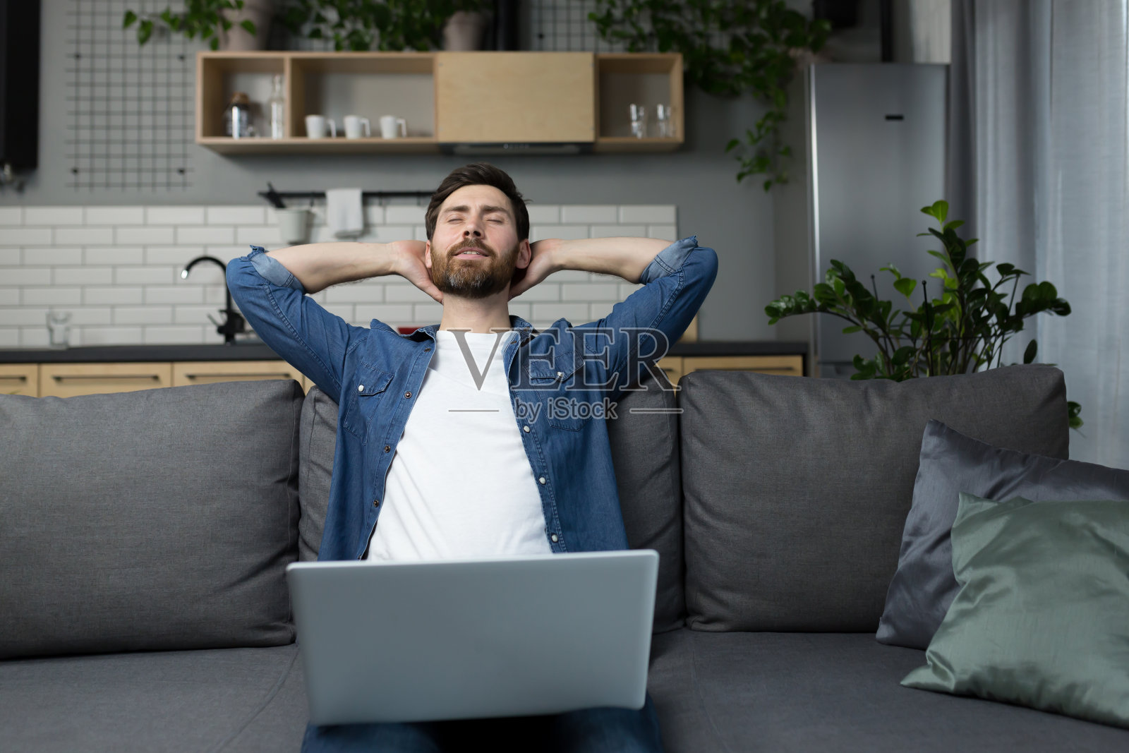 在家的男子坐在沙发上用笔记本电脑工作，双手放在脑后打瞌睡照片摄影图片
