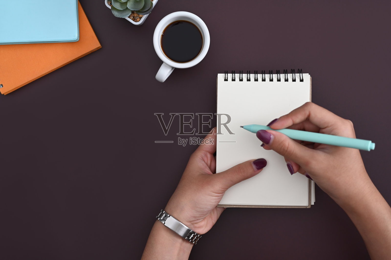 上图是一个时尚的女人拿着钢笔在空白的记事本上写字。照片摄影图片