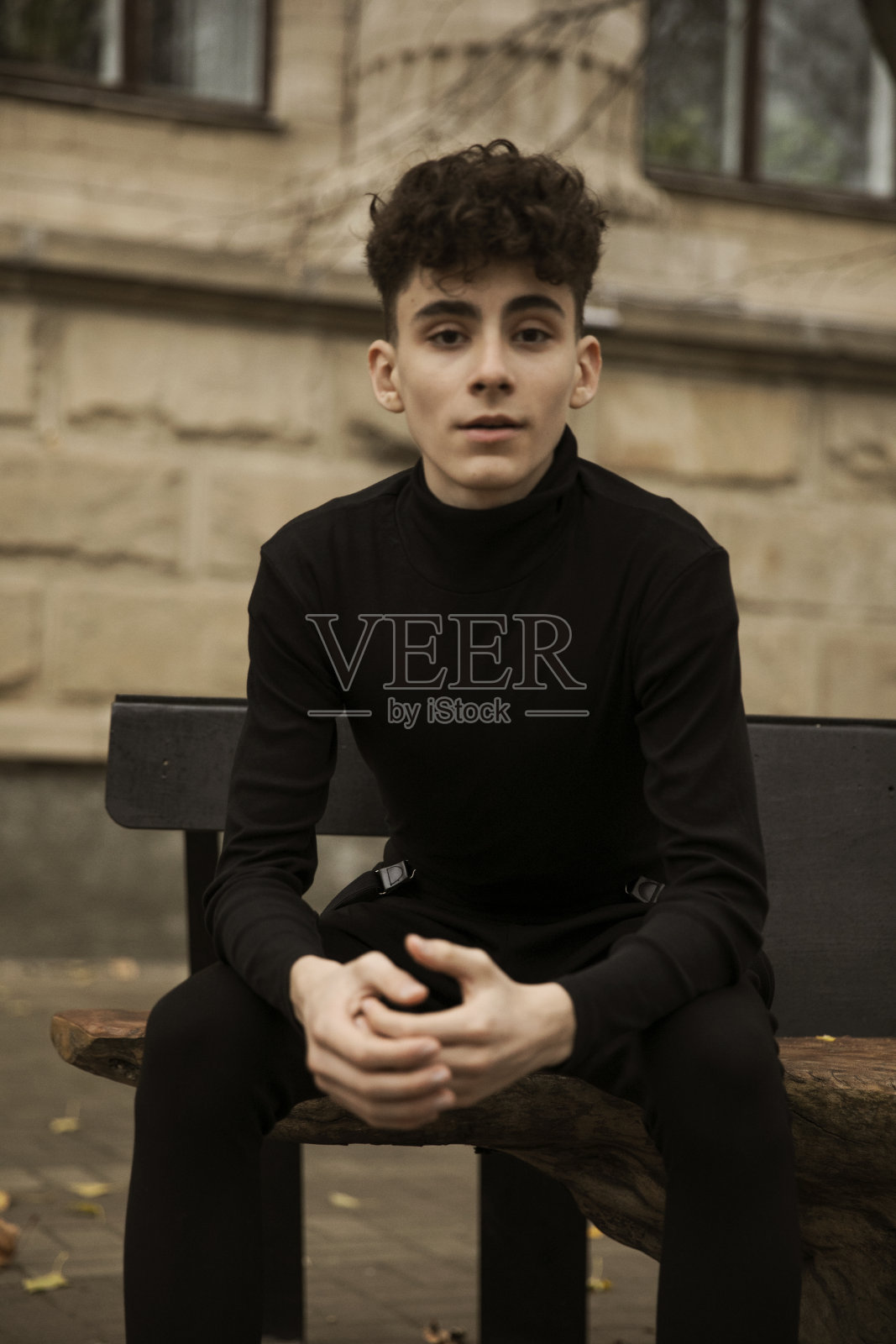 正面照片是一个穿着黑色衣服的年轻男性模特，在一幢建筑后面摆姿势，留着现代发型。照片摄影图片