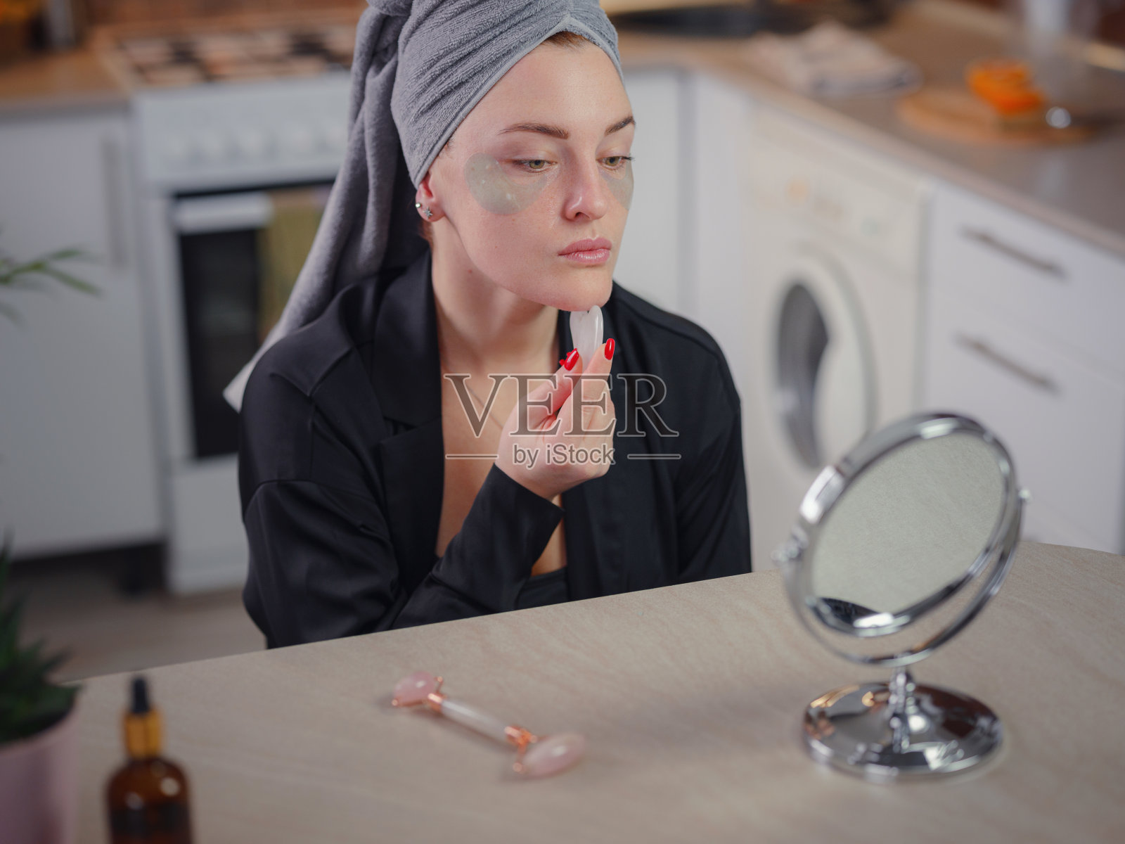 年轻女子在家用面部刮痧玉板照镜子。照片摄影图片