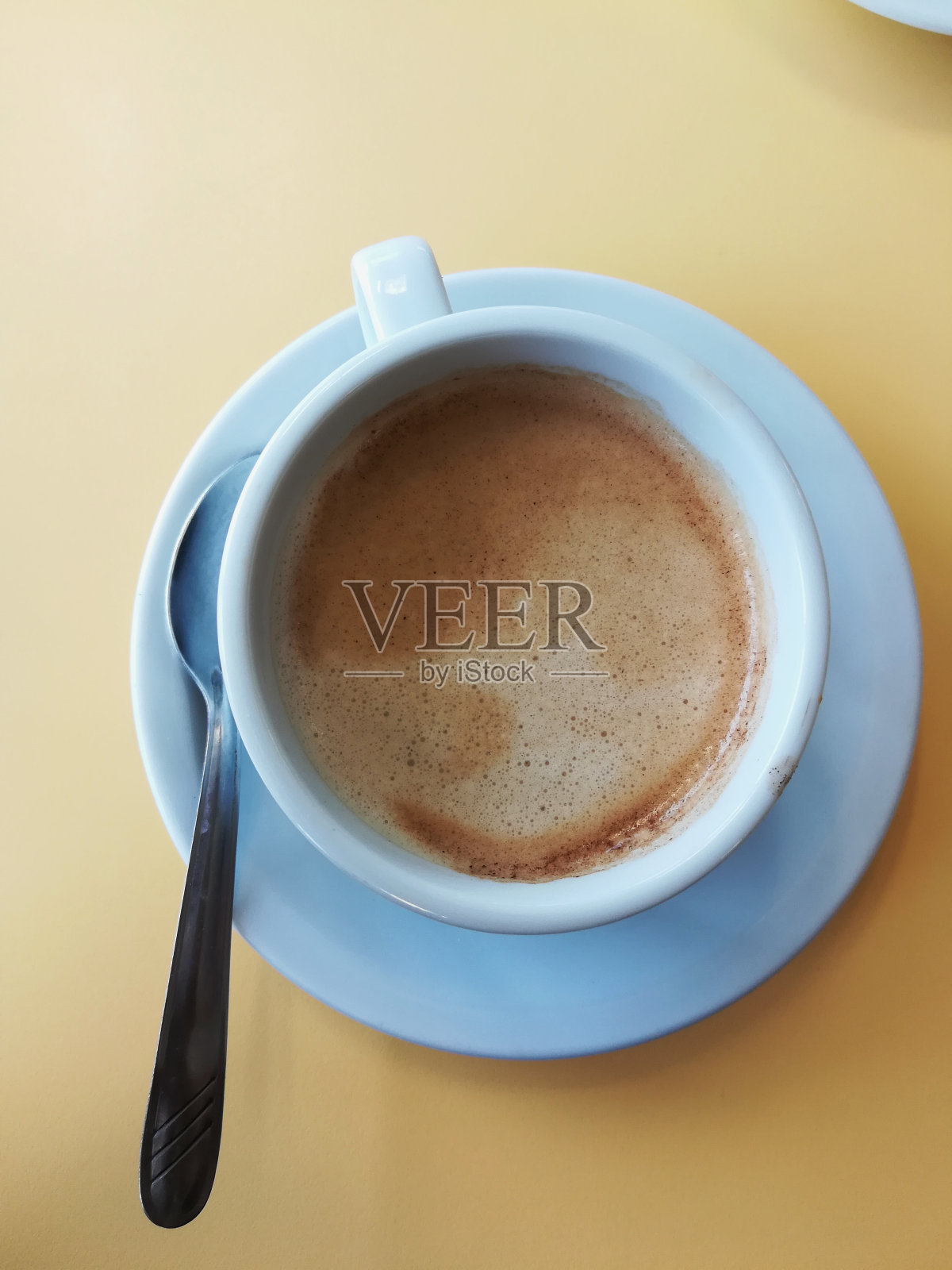 一杯简单的白色卡布奇诺，勺子在旁边，放在一张从上面看是黄色的桌子上照片摄影图片