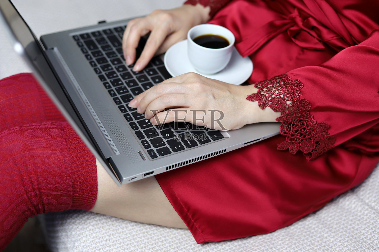一个穿着红色及膝袜和丝绸睡衣的女人坐在沙发上，手里拿着笔记本电脑和咖啡杯照片摄影图片