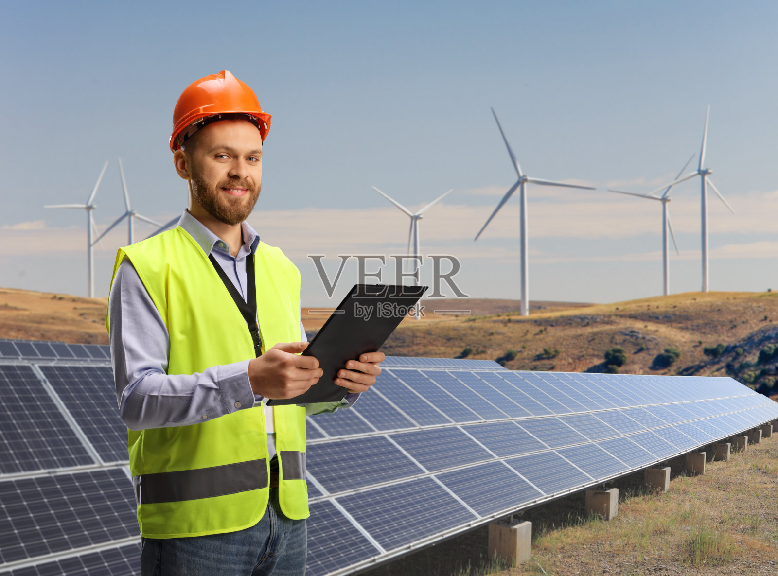 工程师拿着剪贴板在一个可持续的太阳能和风力涡轮机农场上照片摄影图片