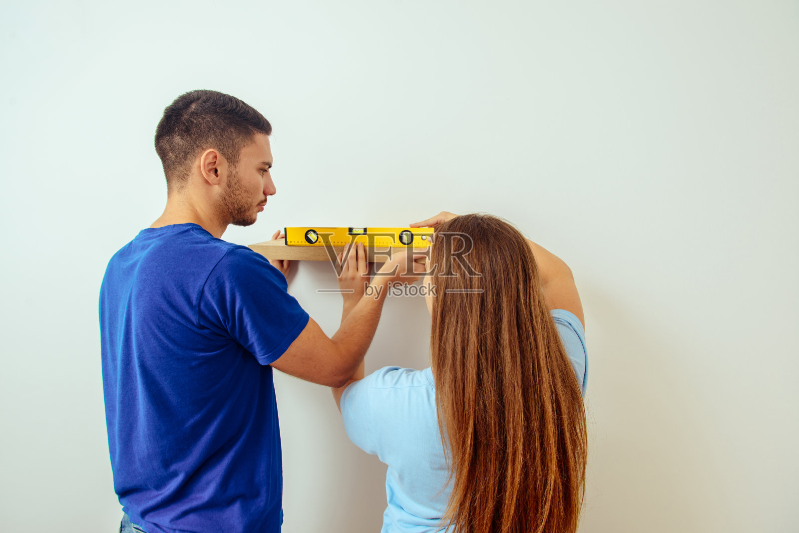 年轻的一家人一起在白墙上安装书架照片摄影图片