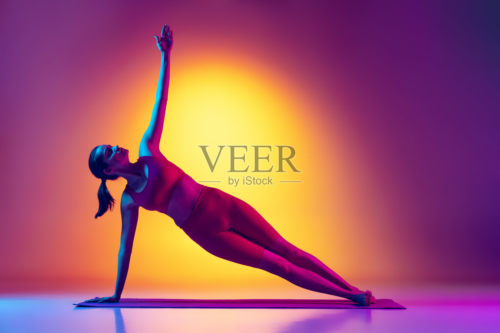 年轻的健康女孩做瑜伽伸展运动的肖像，站在侧板孤立的梯度粉红色和黄色霓虹灯背景照片摄影图片