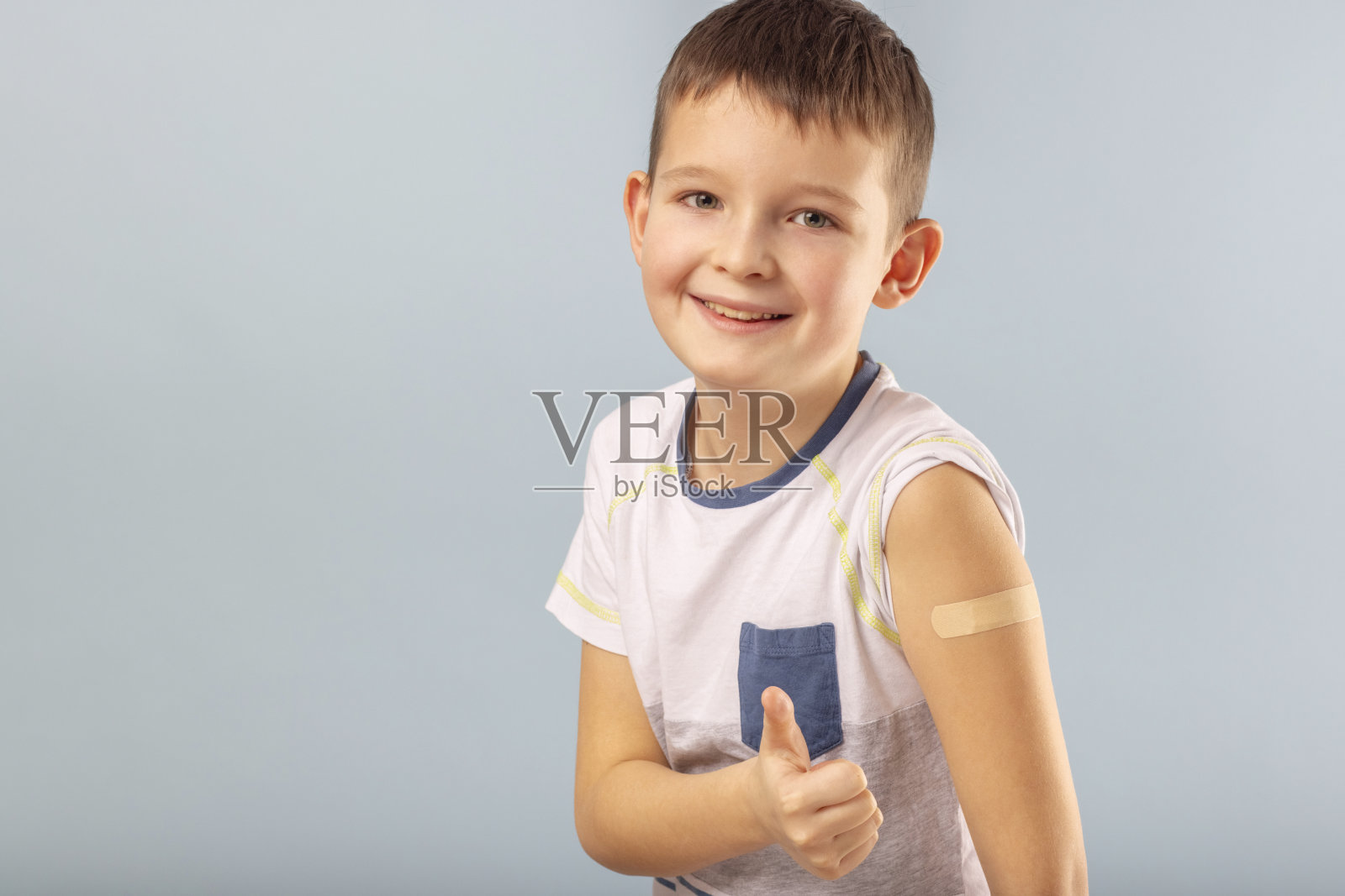 接种疫苗的男孩在注射完冠状病毒疫苗后竖起大拇指，露出打了石膏的手。开始为儿童和青少年接种疫苗。成功Covid-19疫苗接种照片摄影图片