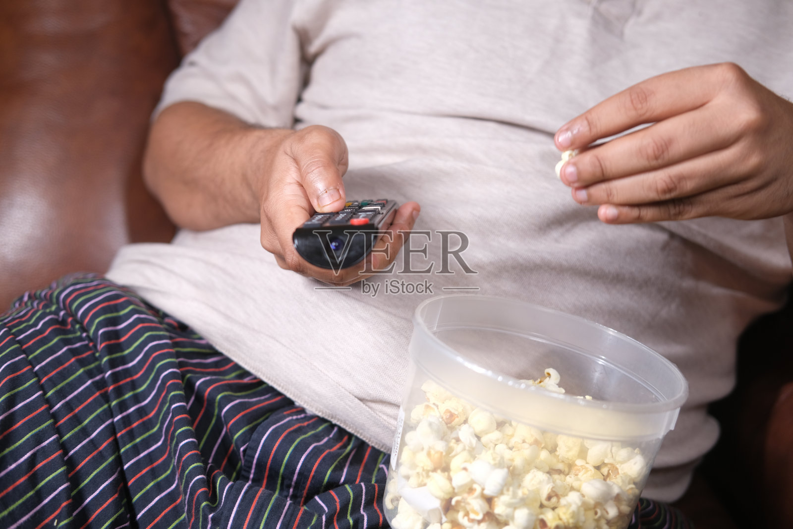 一个胖子拿着电视遥控器坐在沙发上吃着爆米花照片摄影图片