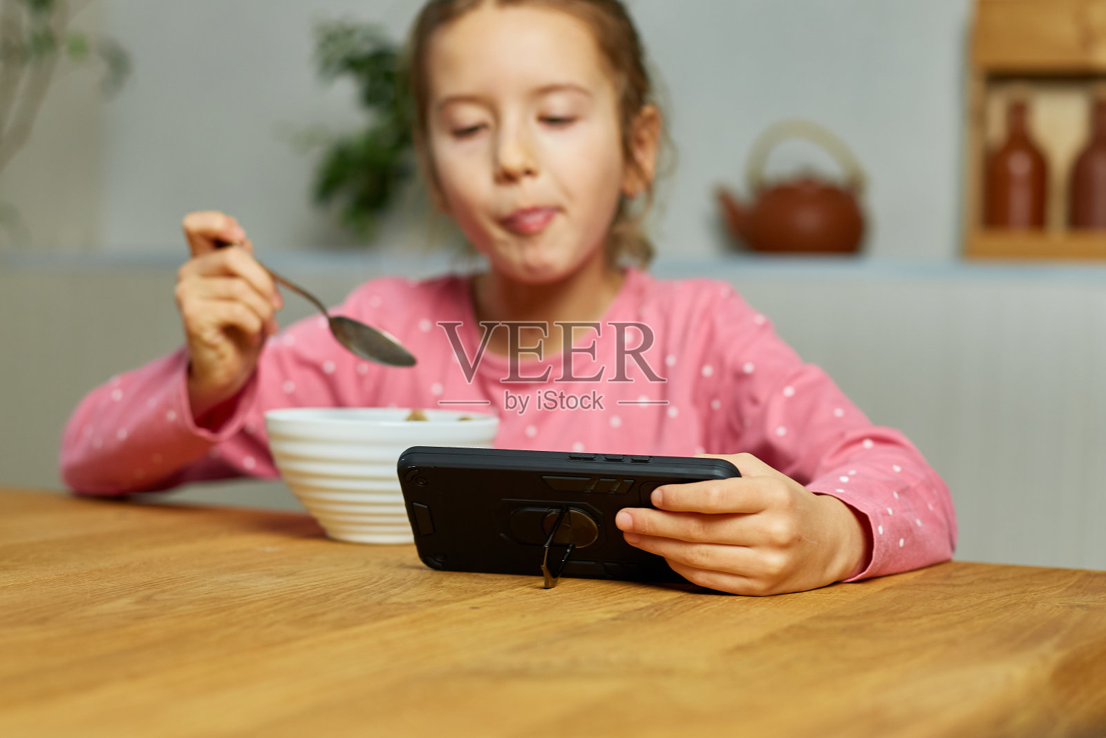 小女孩喝着牛奶吃麦片，用智能手机看视频照片摄影图片