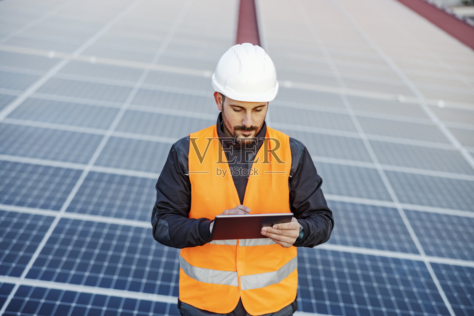 一名专注的工人在平板电脑上测试太阳能电池板的肖像。照片摄影图片