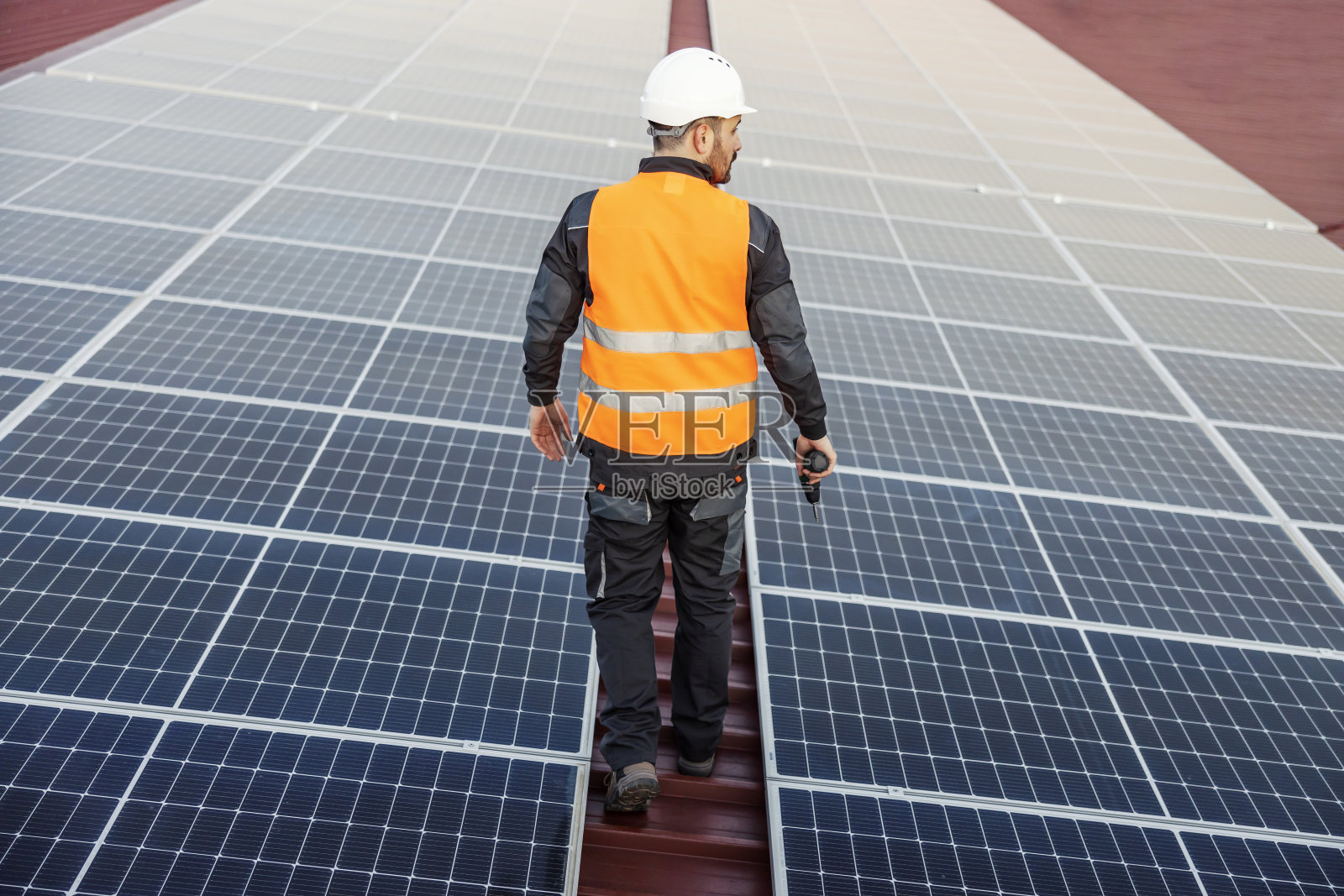 一名工人在屋顶的太阳能电池板之间走来走去，准备修理它。照片摄影图片