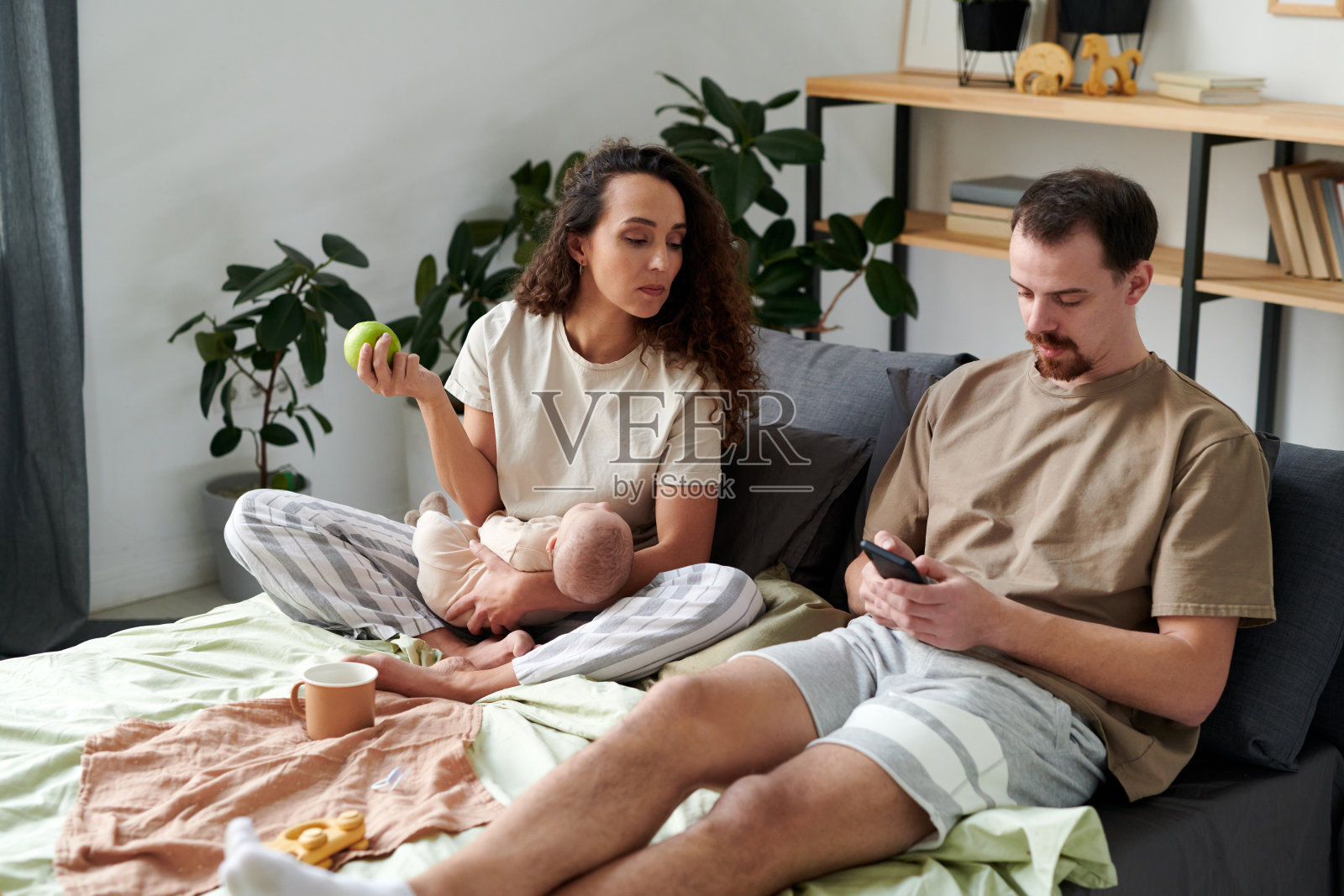 年轻女子看着坐在她旁边的丈夫的智能手机屏幕照片摄影图片