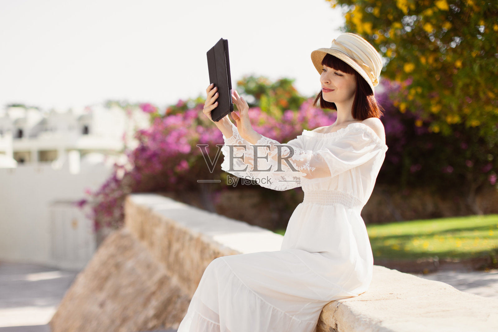 一名年轻女子坐在盛开的热带城市的背景下，用平板电脑拍照照片摄影图片