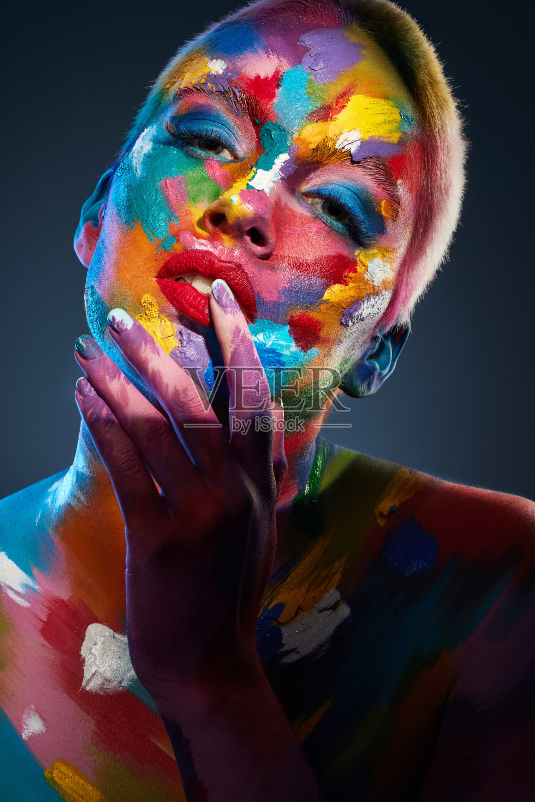 这是一名年轻女子脸上涂着彩色颜料摆姿势的画室照片照片摄影图片