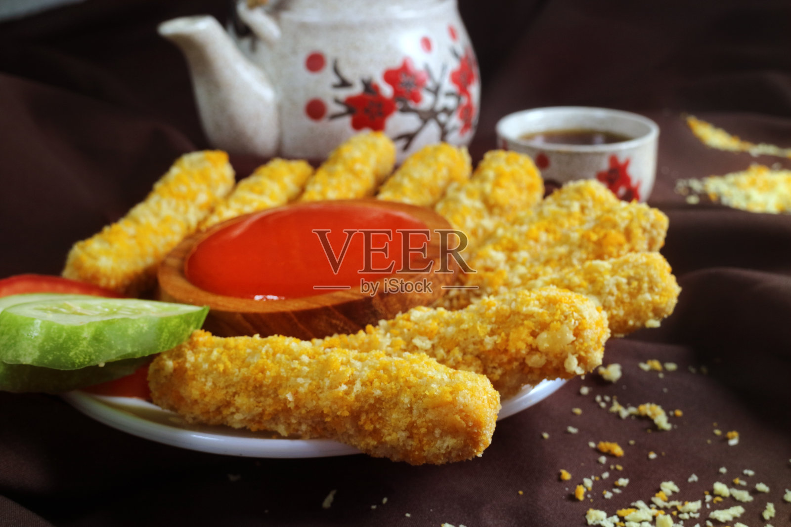 鸡块、薯条、炸鱼、黄瓜、番茄酱、茶壶、棕色布背景的微距离镜头照片摄影图片