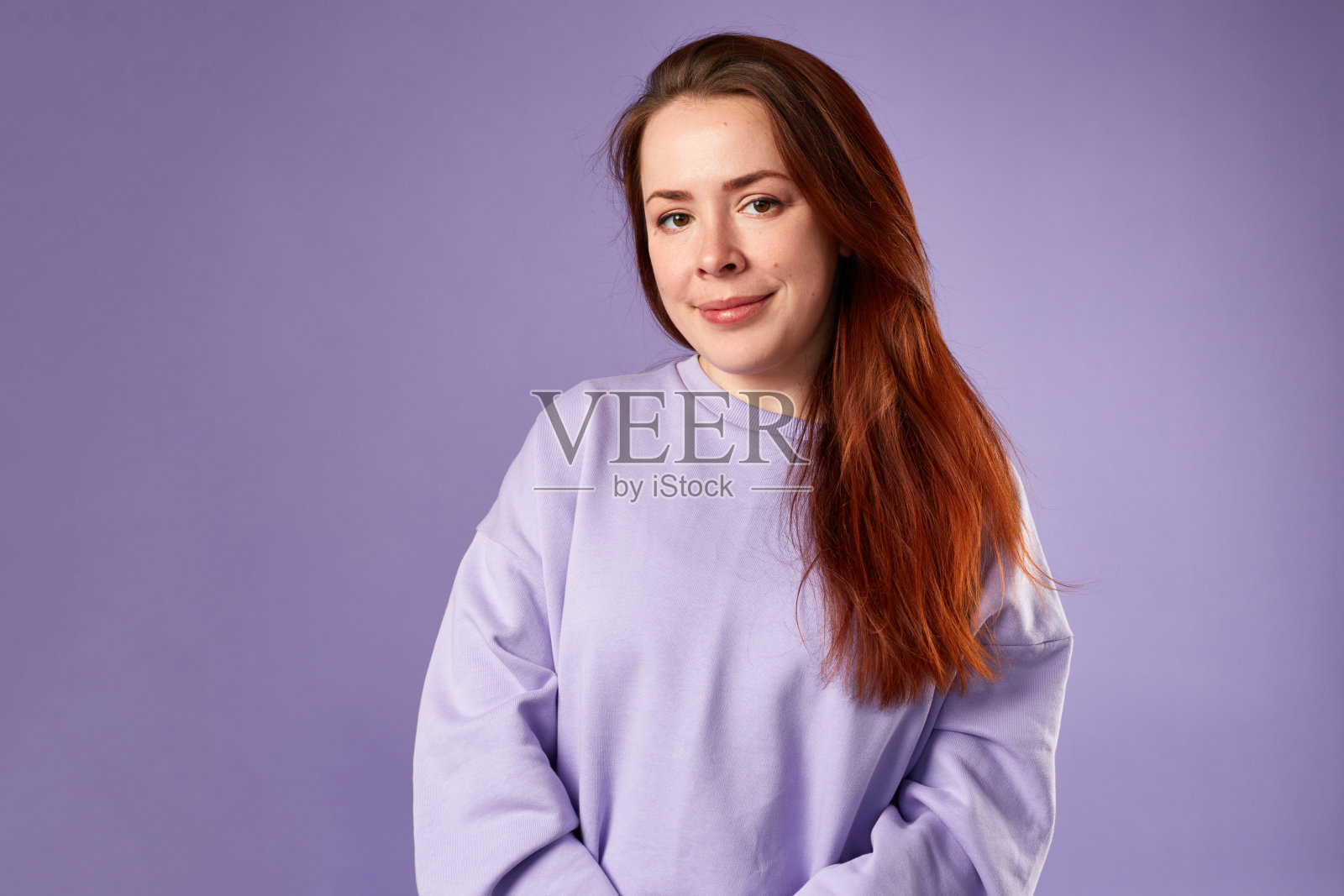 穿紫色运动衫的白人妇女。自然的外观。面带微笑。红色的长发。紫色的背景照片摄影图片