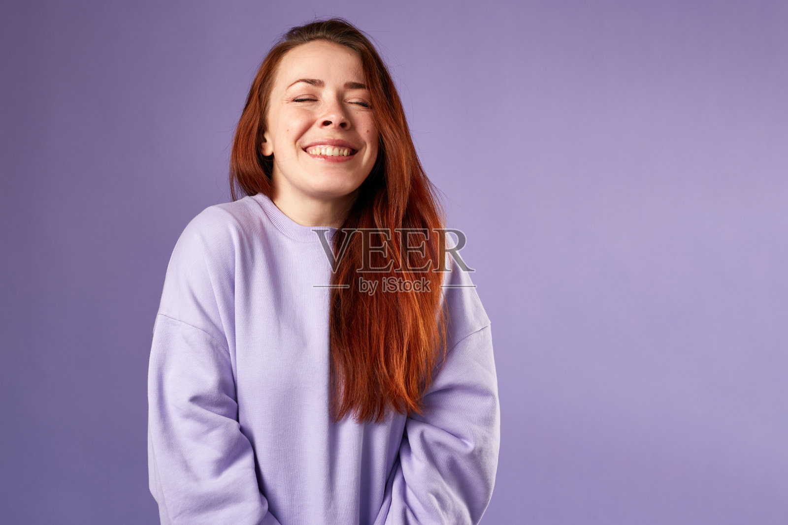 穿紫色运动衫的白人妇女。自然的外观。面带微笑。红色的长发。紫色的背景照片摄影图片