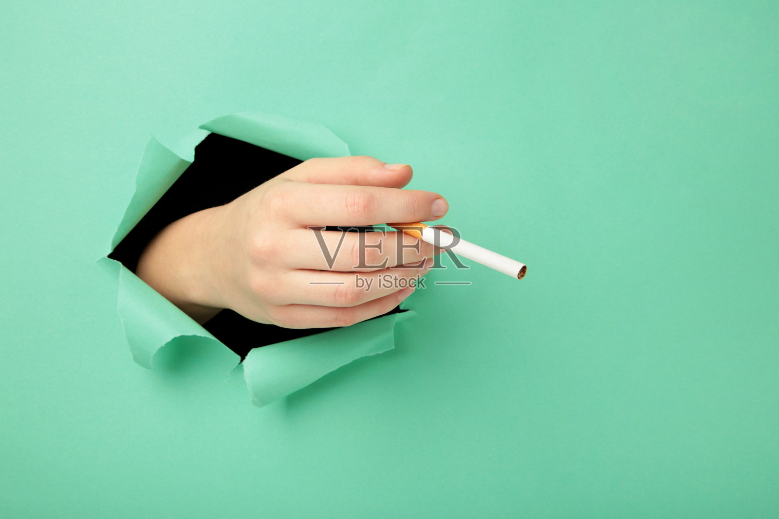 一个女人手里拿着一支香烟，薄荷色的背景。侧视图，水平，有复制空间。照片摄影图片