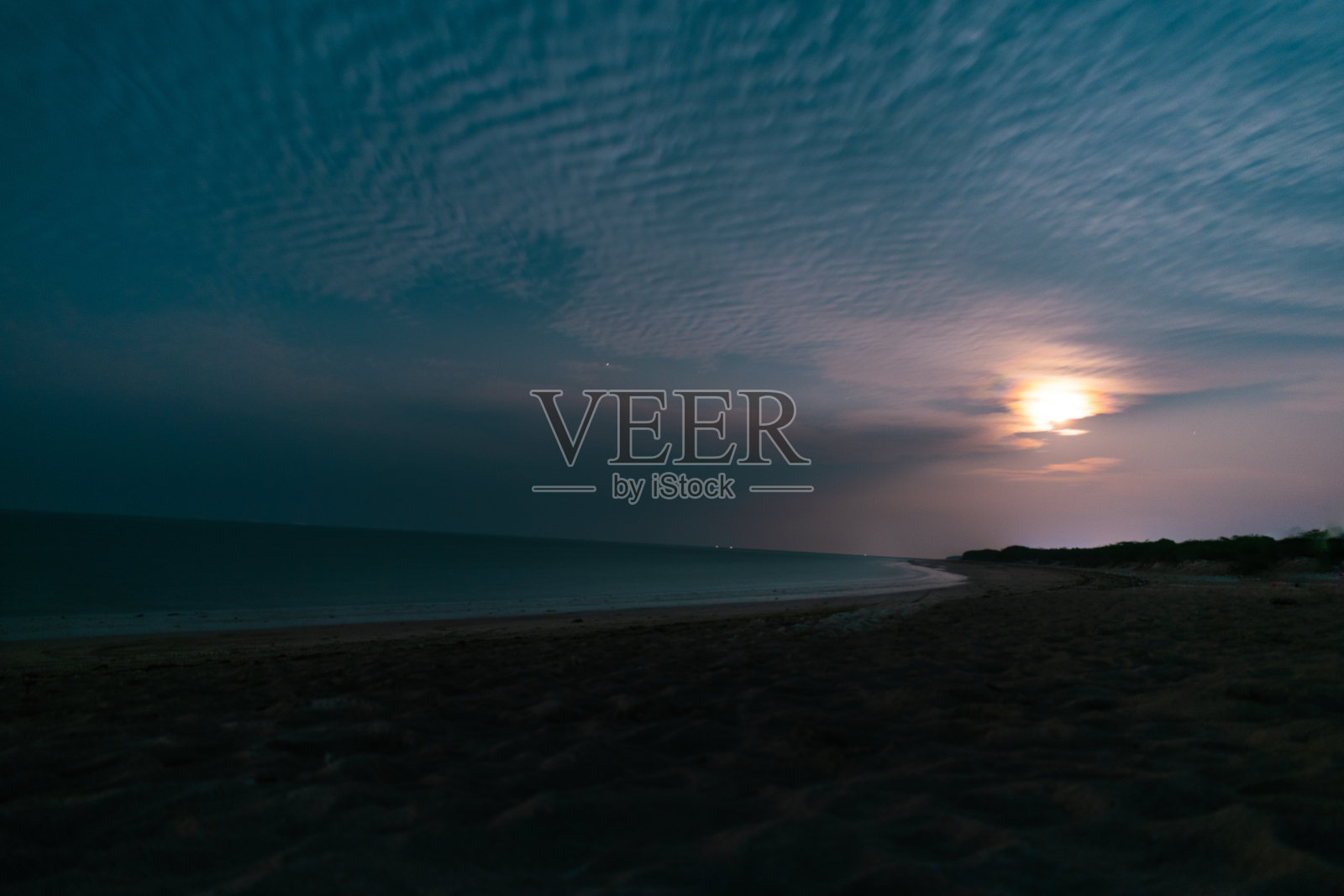 月亮在多云的沙滩上升起。夜间海洋的长曝光镜头。热带海滩的夏日假期背景。宁静的自然背景。照片摄影图片