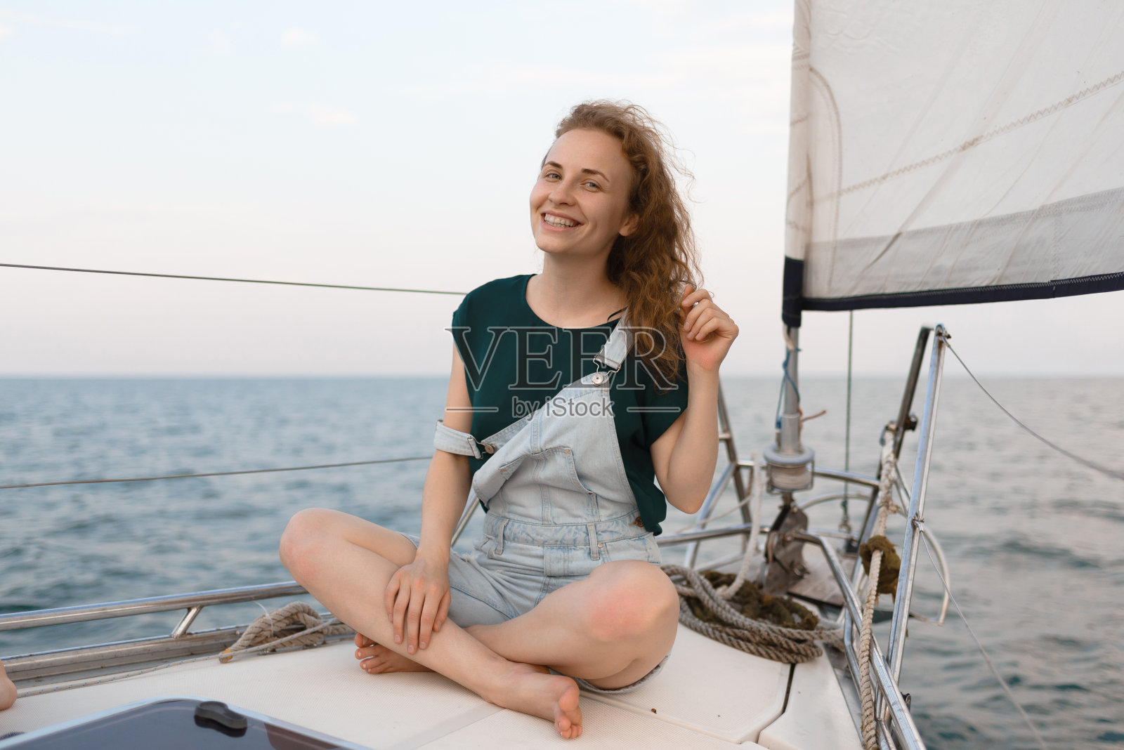 一位迷人的女子坐在游艇上，面带微笑地看着镜头，抚摸着自己的红头发照片摄影图片