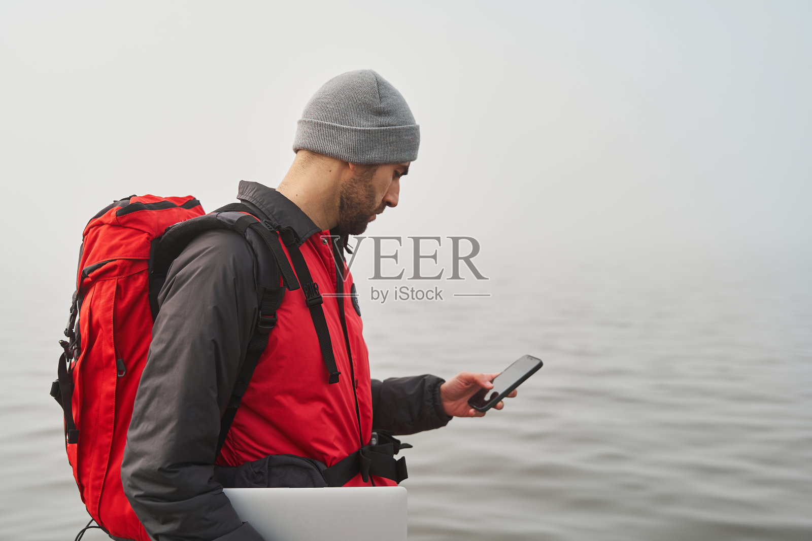 工作自由的理念。男性旅行背包和笔记本电脑在海边检查手机照片摄影图片