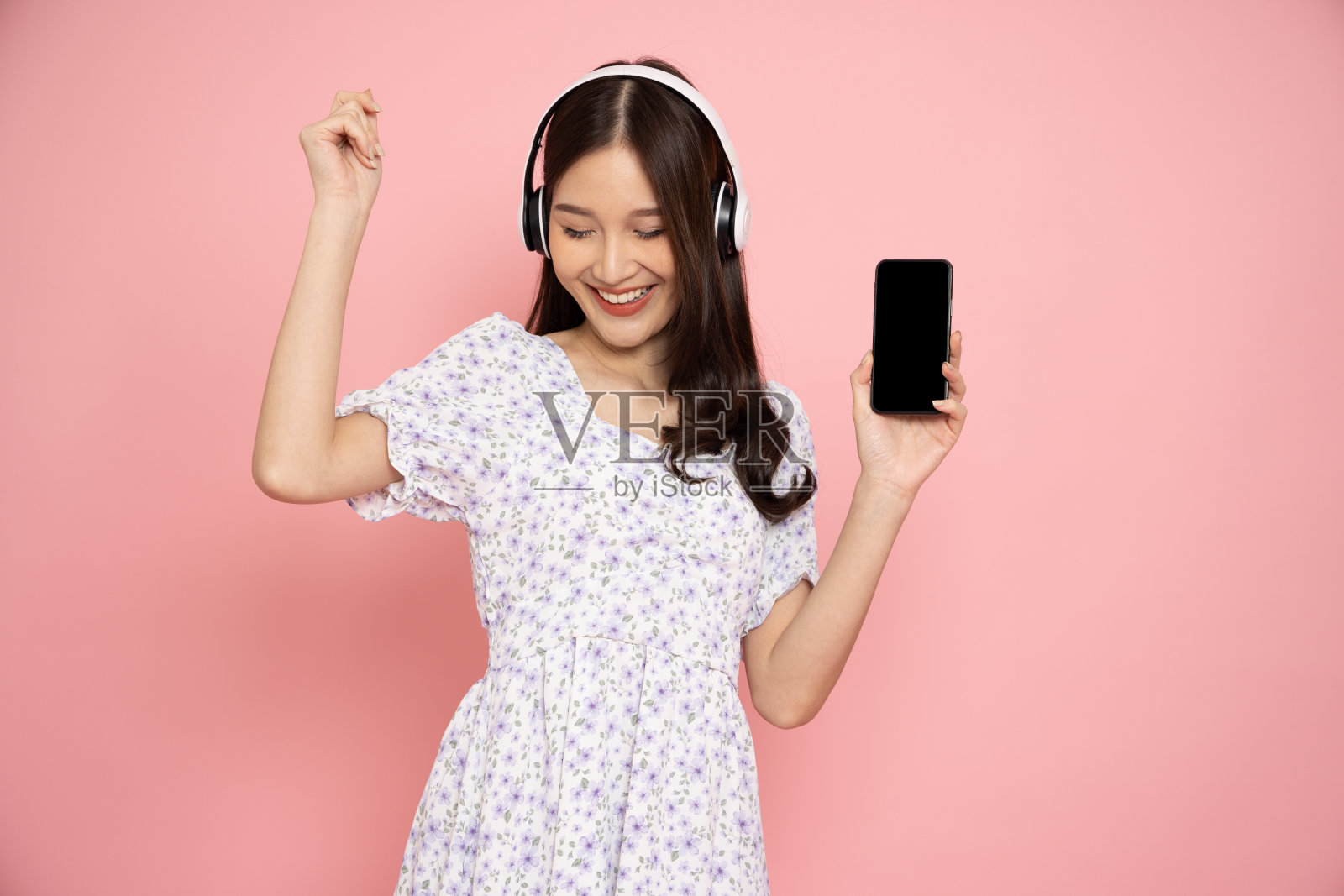 年轻的亚洲妇女听最喜欢的音乐在移动电话应用程序与无线耳机和跳舞孤立在粉红色的背景照片摄影图片