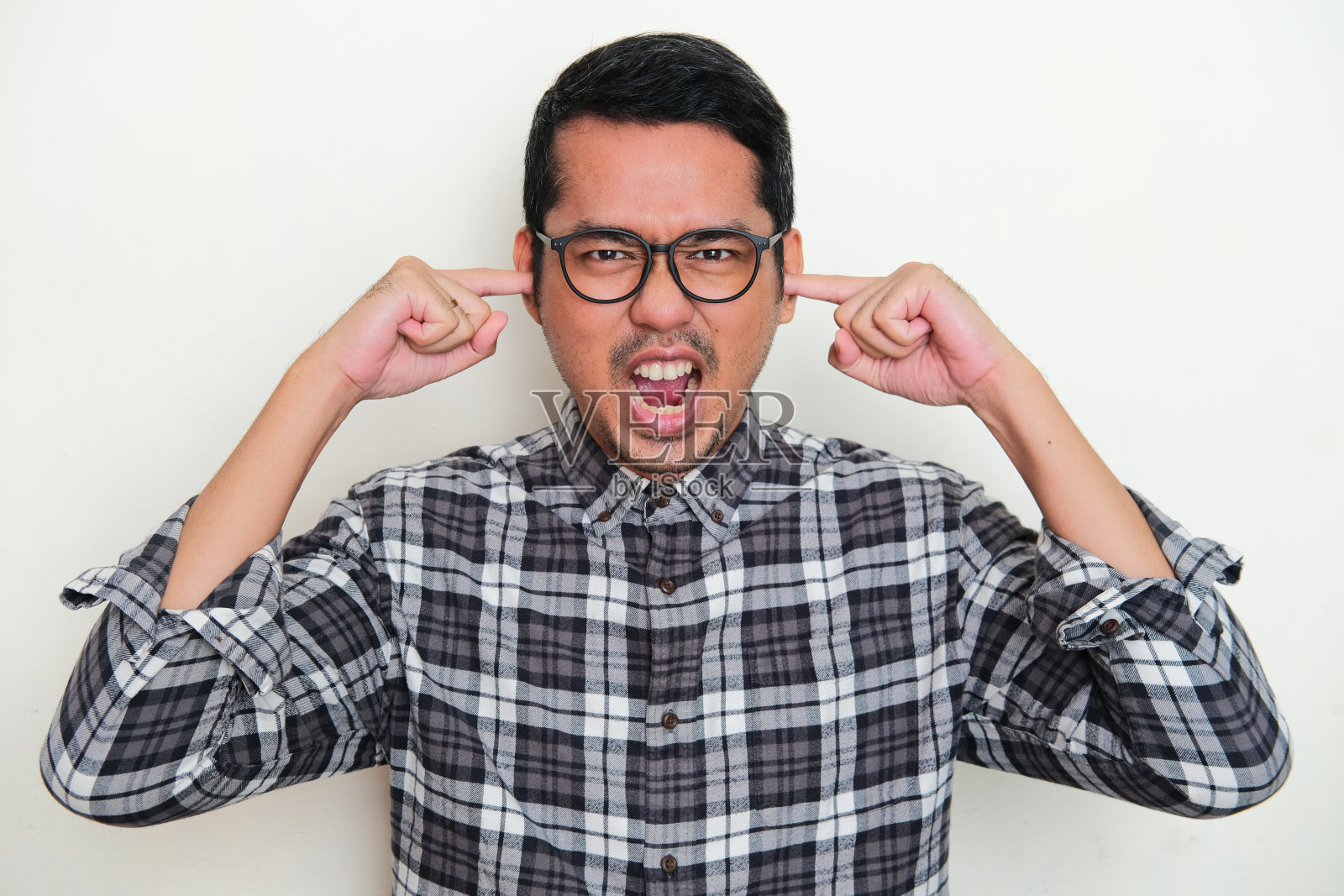 亚洲成年男子尖叫愤怒的肖像，同时用手指关闭他的耳朵照片摄影图片