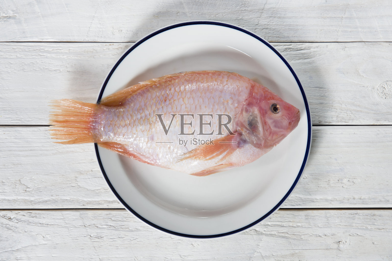 新鲜的粉色罗非鱼，放在木制的白色桌子上的盘子里，生的食物，自然的背景，彩色的食物平铺，照片摄影图片