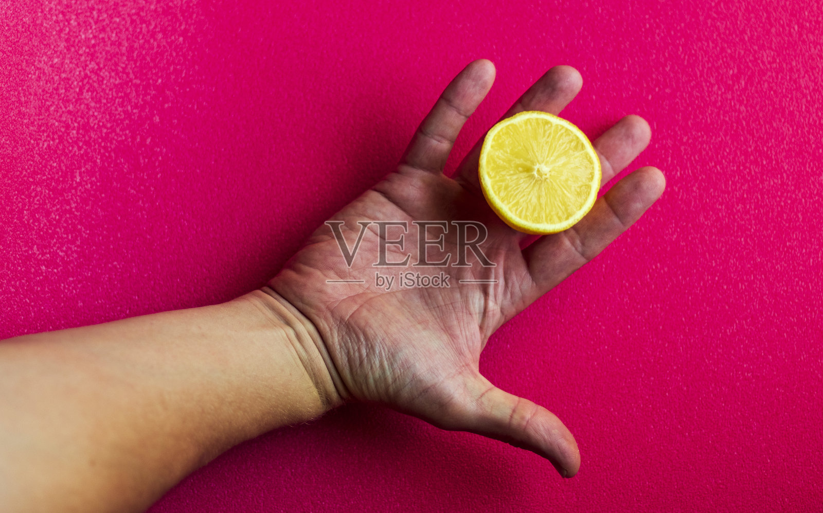 手持切成两半的柠檬，粉红色背景。食物照片摄影图片