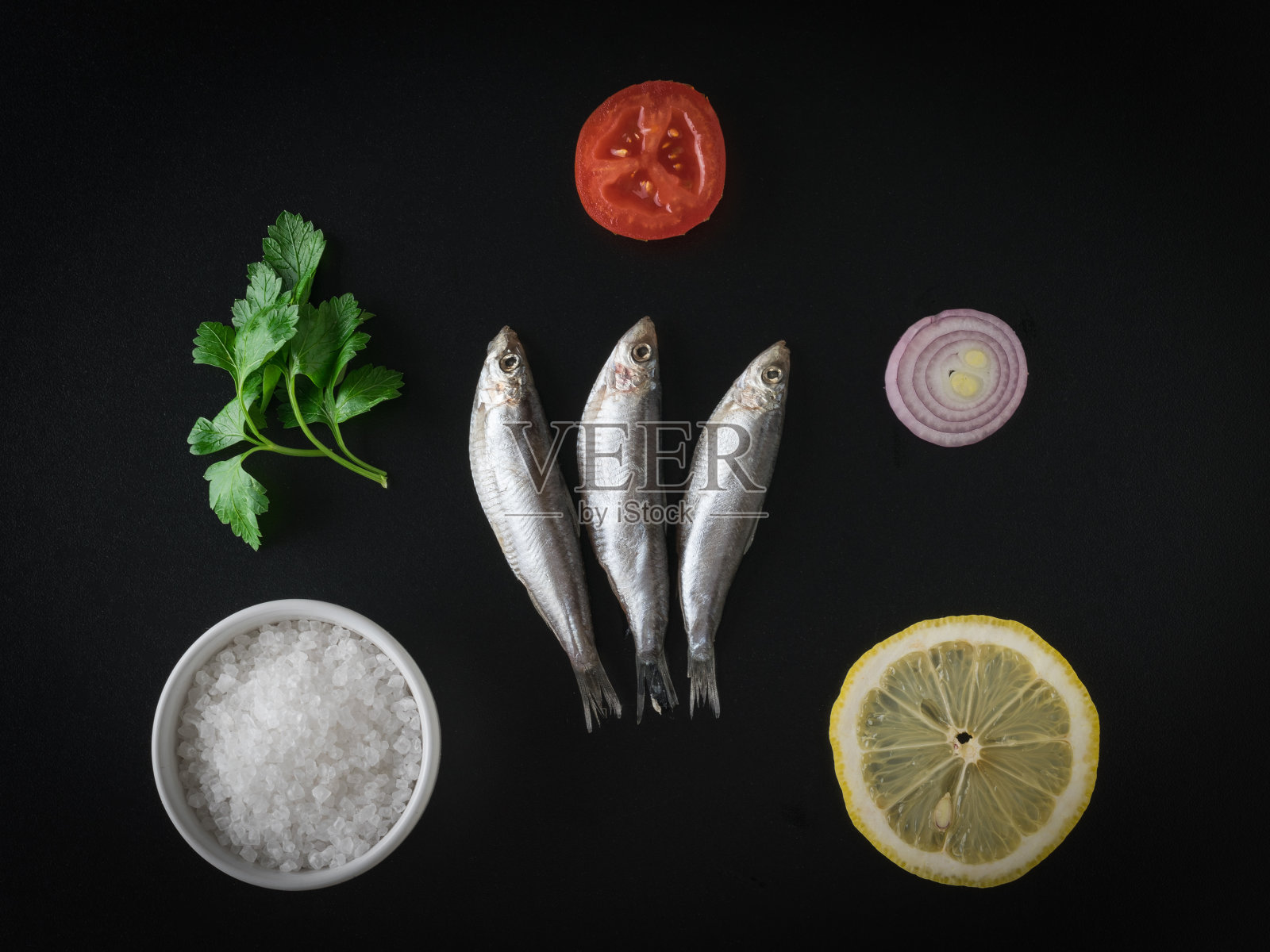 在黑色的桌子上放上盐腌的鲱鱼、洋葱、番茄、欧芹和柠檬。平的。照片摄影图片