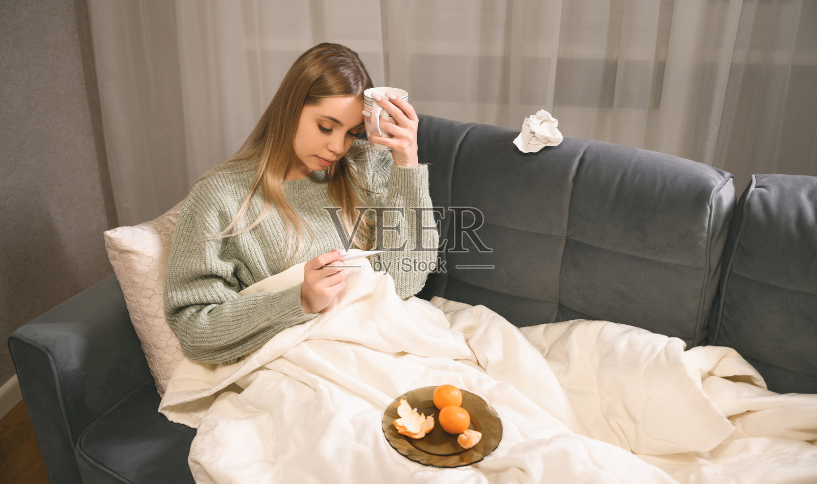 精疲力竭的女人生病了，躺在床上拿着温度计检查体温。生病的金发女孩躺在床上照片摄影图片