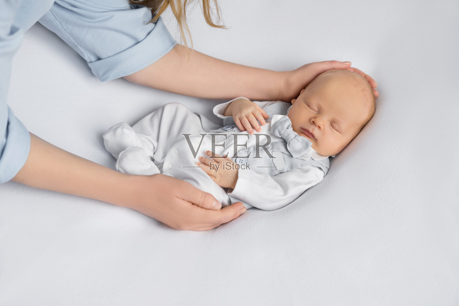 妈妈的手抱着睡在浅色背景上的西装新生男婴。快乐的怀孕和分娩。儿童主题。俯视图照片摄影图片